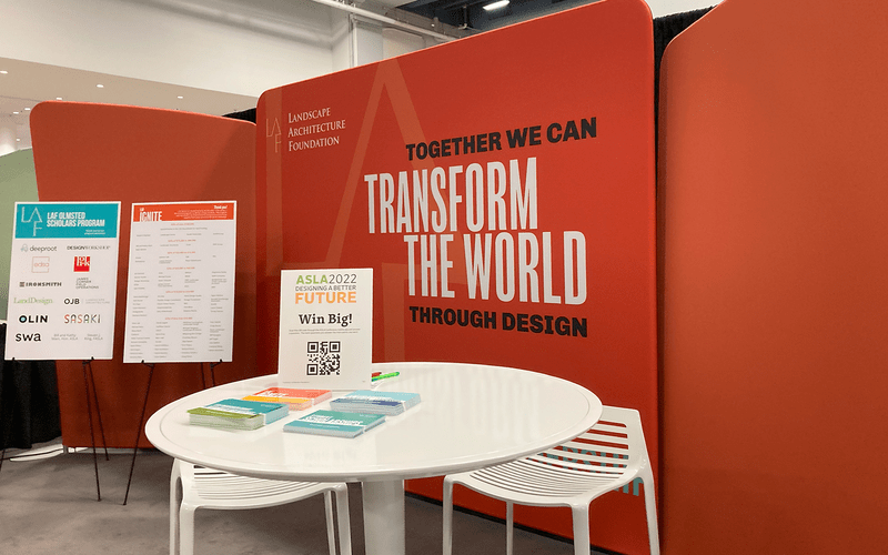 LAF EXPO booth with a white table and postcards in front of a coral red backdrop